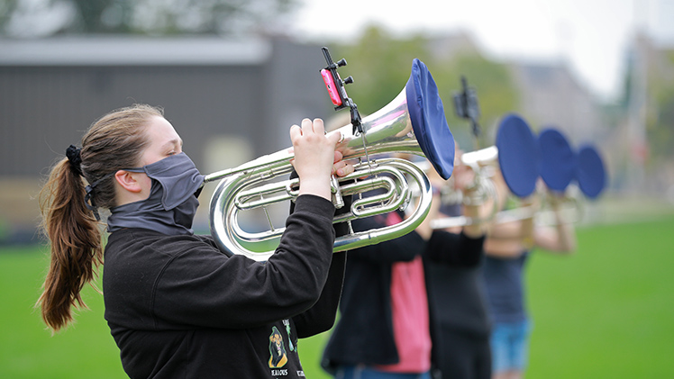 Marching band members playing brass horns with special coverings
